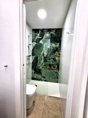 Un baño con cabina de ducha de vidrio, inodoro y bañera con revestimiento similar al mármol.