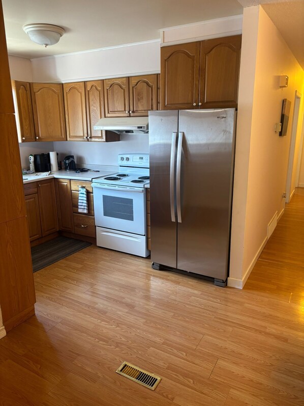 Una cocina con armarios de madera, un refrigerador de acero inoxidable, una estufa blanca y una campana extractora.