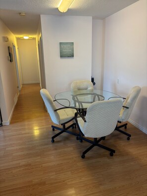 A conference room with a glass table and four chairs, a hallway leading to another room, and a wall-mounted sign.