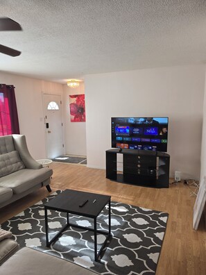 A living room with a sofa, a coffee table, a TV on a stand, a patterned rug, and a door with a window.