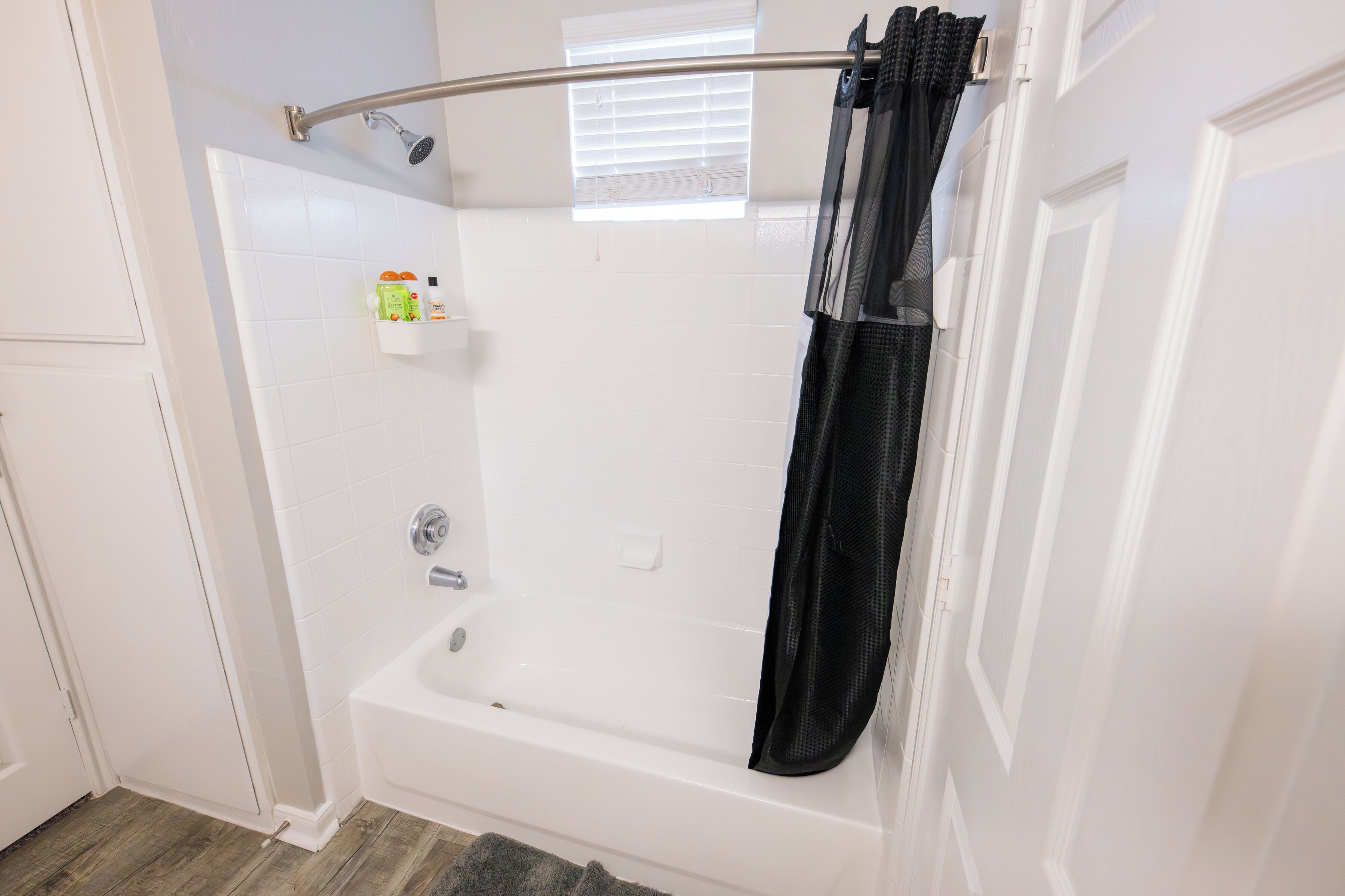 A bathroom with a bathtub, a shower, and a window with blinds.