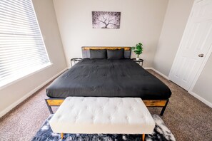 Ein Schlafzimmer mit einem großen Bett, einem Nachttisch mit Pflanze und einer Tür.