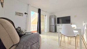 Una sala moderna con sofá, comedor con mesa y sillas, televisor y balcón con barandilla.