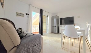 Ein modernes Wohnzimmer mit Sofa, Essbereich mit Tisch und Stühlen, Fernseher und Balkon mit Geländer.
