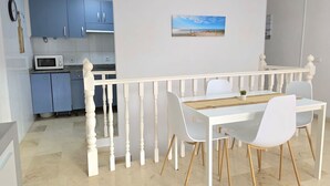 Un área de comedor con una mesa y sillas blancas, una baranda blanca y una cocina al fondo.