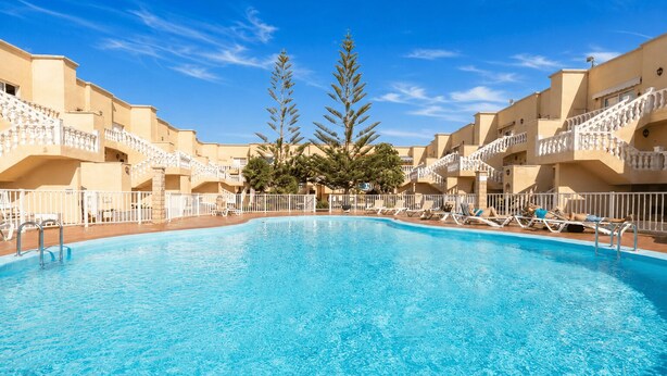 Una piscina rodeada de edificios de varios pisos con balcones, árboles y un cielo azul despejado.