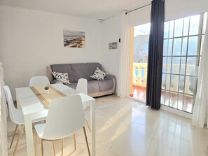 Un salon avec un canapé, une table à manger et des chaises, une fenêtre avec des rideaux et une vue sur l’extérieur.