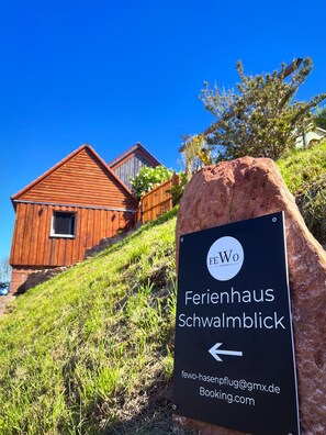 Edificio de madera con un letrero que indica 'Ferienhaus Schwalmblick' y una flecha señalando a la izquierda.