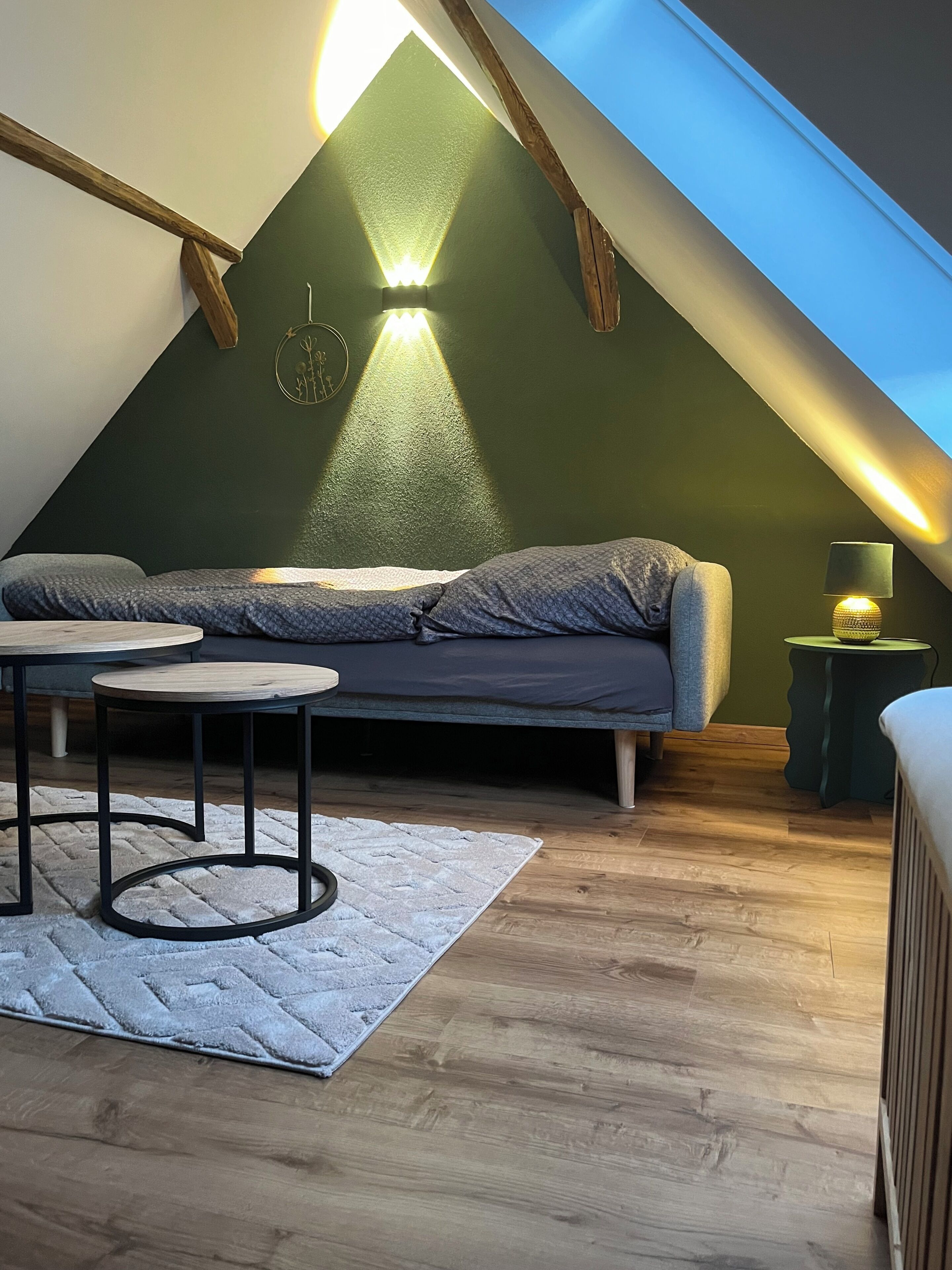 Een gezellig slaapkamer onder het dak, met schuine wanden, een bed, een klein tafeltje en een lamp.