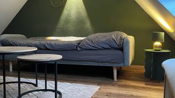 Een gezellig slaapkamer onder het dak, met schuine wanden, een bed, een klein tafeltje en een lamp.