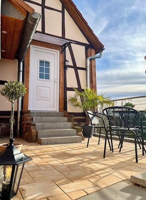 Un bâtiment avec une porte blanche, des marches en pierre, un balcon avec des chaises et des plantes en pot.
