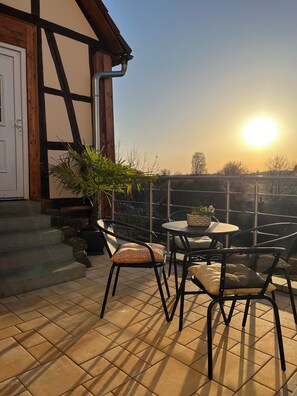 Una terraza con mesa y sillas, una planta en maceta y vistas al atardecer.