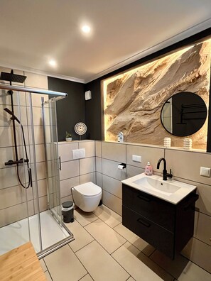 Een moderne badkamer met een douchecabine van glas, een wit toilet, een wastafelmeubel en een decoratieve wand met een reliëfpatroon.