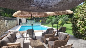 A poolside area with wicker furniture, a stone wall, and a view of a swimming pool. - La Bastide perched village in the Luberon (Ménerbes)