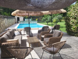 A poolside area with wicker furniture, a stone wall, and a view of a swimming pool. - La Bastide perched village in the Luberon (Ménerbes)