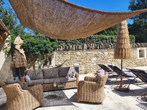Een zonnig terras met rieten meubels, een stenen muur en een rieten parasol.