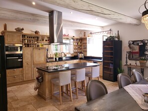 A modern kitchen with wooden cabinets, a central island with chairs, a built-in oven, and a stainless steel range hood. - La Bastide perched village in the Luberon (Ménerbes)