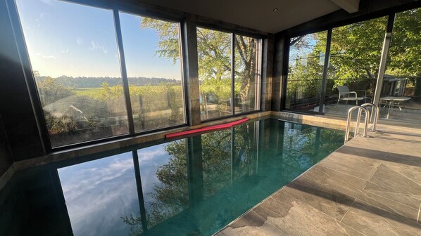 Une piscine intérieure avec des parois en verre transparent, une ligne de sécurité rouge et une vue sur les arbres et les collines.