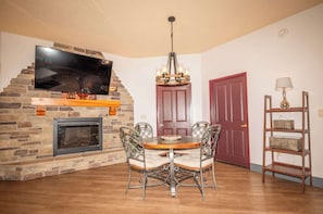 A dining area with a brick fireplace, a flat-screen TV, a chandelier, and a red door.