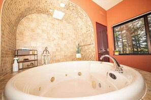 Ein Badezimmer mit freistehender Badewanne, einer Dusche, einem Waschbecken und einem Fenster mit Blick auf Bäume.