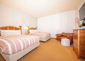 Ein Hotelzimmer mit zwei Betten, einem braunen Ledersofa, einem Holzschrank und einem kleinen runden Hocker.