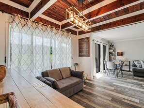Una sala de estar moderna con techo de madera, un sofá gris, una mesa de comedor de madera y una cocina al fondo.