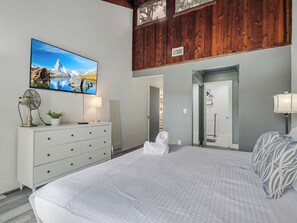 Ein Schlafzimmer mit Bett, Kommode, Ventilator, Fernseher und einer Tür zum Badezimmer.