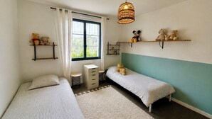 Ein Schlafzimmer mit zwei Betten, einem Fenster mit Vorhängen, einer Hängeleuchte und Regalen mit Stofftieren.