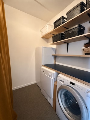 A compact laundry area with a washing machine, dryer, and shelves with baskets. - Elegant house with heated pool in Dinard - 6 people (Dinard)