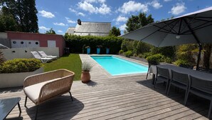 Eine Holzterrasse mit Pool, Liegestühlen und Sonnenschirm.