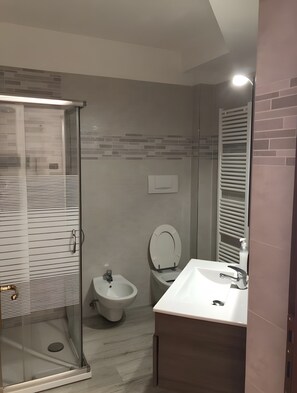 Un bagno moderno con cabina doccia in vetro, un bidet, un water e un lavabo con specchio.