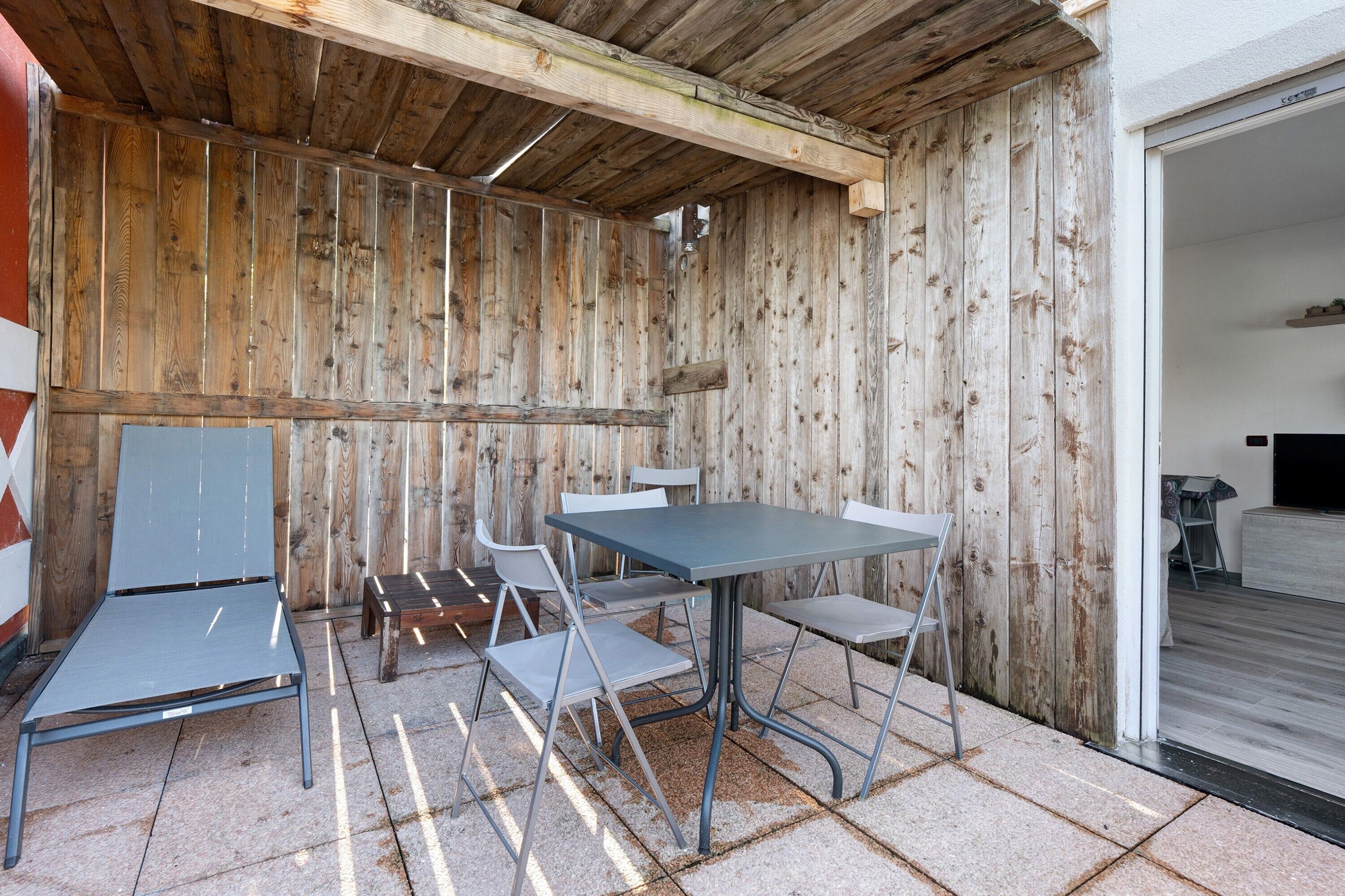 An outdoor patio with a wooden wall, a table, and four chairs.