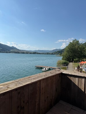 Un muelle de madera se extiende sobre un lago, con un bote amarrado al final, rodeado de vegetación y colinas lejanas.
