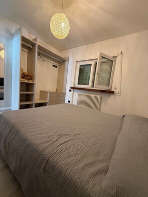 Ein Schlafzimmer mit Bett, Schrank, Heizkörper und einem Fenster mit Jalousien.