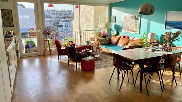 A spacious living area with a dining table, sofa, and chairs, a balcony with plants, and a city view. - Spacious, bright apartment near Montmartre! Ideal for families. (Paris)