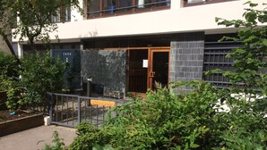 A modern building with a glass door entrance, a metal fence, and a variety of green plants. - Spacious, bright apartment near Montmartre! Ideal for families. (Paris)