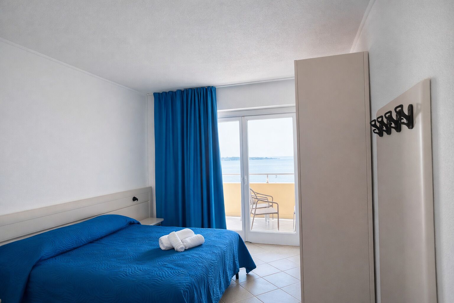 Habitación de hotel con cama, baño y balcón con vistas al mar.