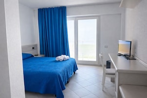 Una camera d'albergo con un letto, una scrivania, una sedia e vista attraverso una porta scorrevole.