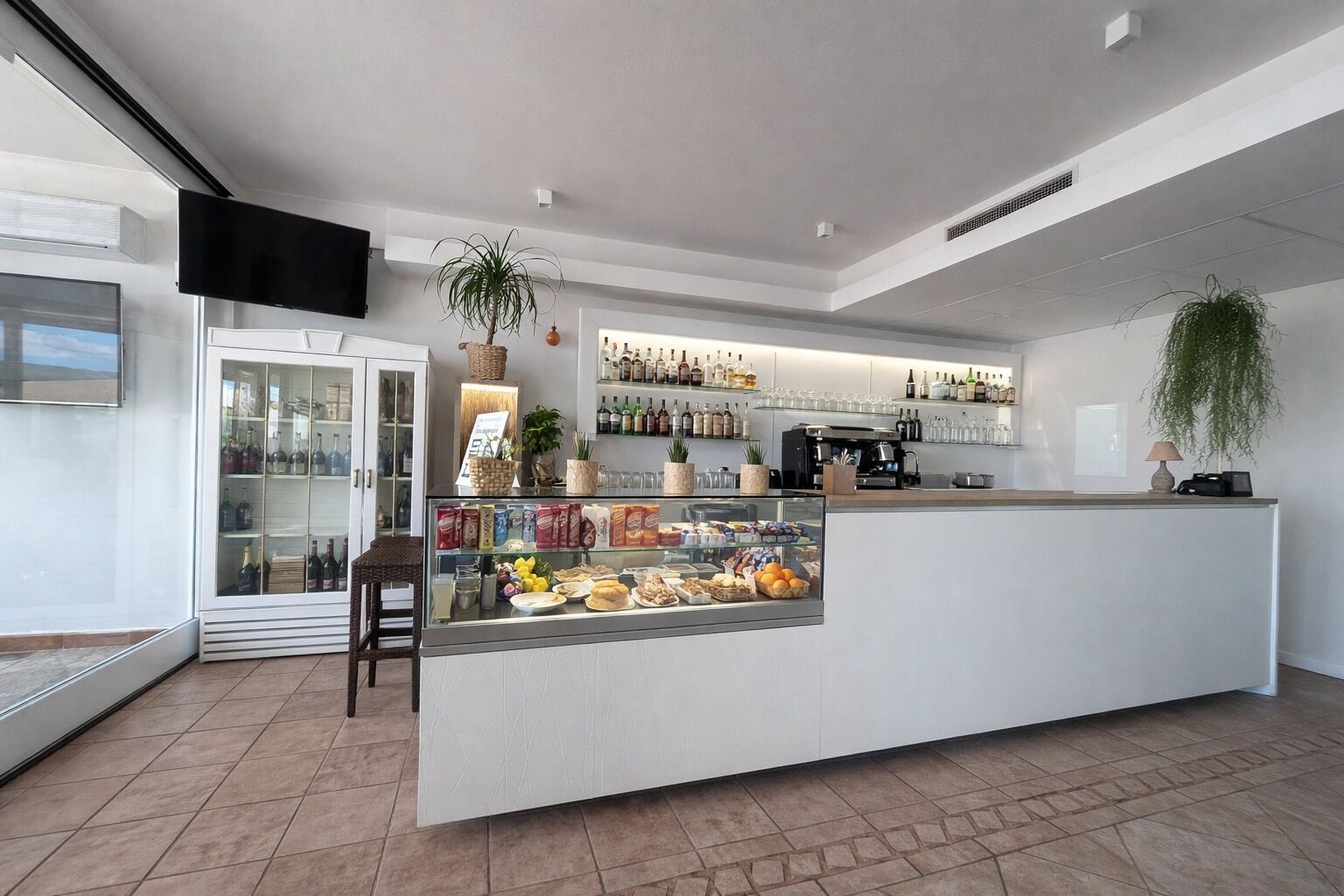 Zona bar moderna con una vetrina in vetro, scaffali pieni di bottiglie e una macchina da caffè.