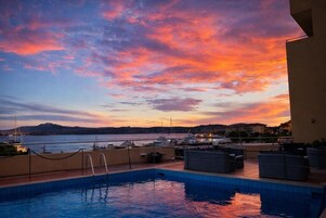 Una piscina con vista sul mare e sulle barche al tramonto.