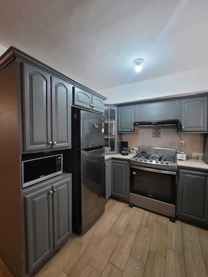 Una cocina con armarios oscuros, un refrigerador de acero inoxidable, un microondas, una estufa a gas y una cafetera.