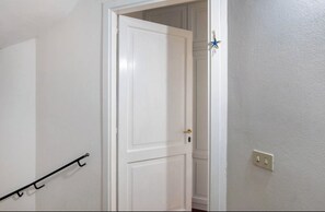 Eine weiße Tür mit goldener Klinke, ein schwarzer Metallregal und ein Lichtschalter an der Wand.