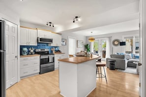 Une cuisine moderne avec des meubles blancs, un îlot central et un coin repas comprenant un canapé gris et une table basse.