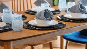 A dining table set with plates, glasses, and napkins, with a chair and a plant in the background.