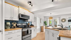 A modern kitchen with white cabinetry, stainless steel appliances, and a wooden countertop.