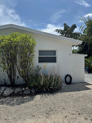 A single-story building with a window and a door, surrounded by gravel and plants. - Furnished, updated 1-bedroom apartment in charming Layton ideal for snow-birds (Layton)