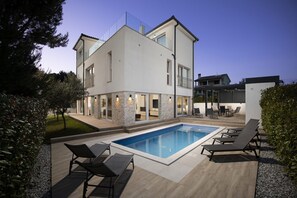 Ein modernes, zweistöckiges Haus mit Schwimmbad, Sitzgelegenheiten im Freien und einem gepflegten Garten.