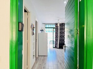 Ein Flur mit einer grünen Tür, einem weißen Kühlschrank und gemusterten Vorhängen.