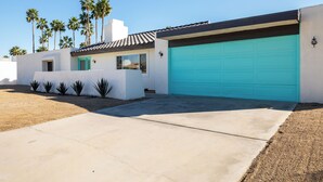 Une maison moderne avec une porte de garage turquoise, une façade blanche et un petit espace patio.