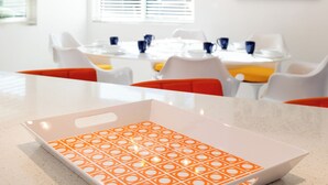 Une cuisine moderne avec un plan de travail blanc, un plateau décoré, un lustre et un coin repas avec des chaises et une table blanches.